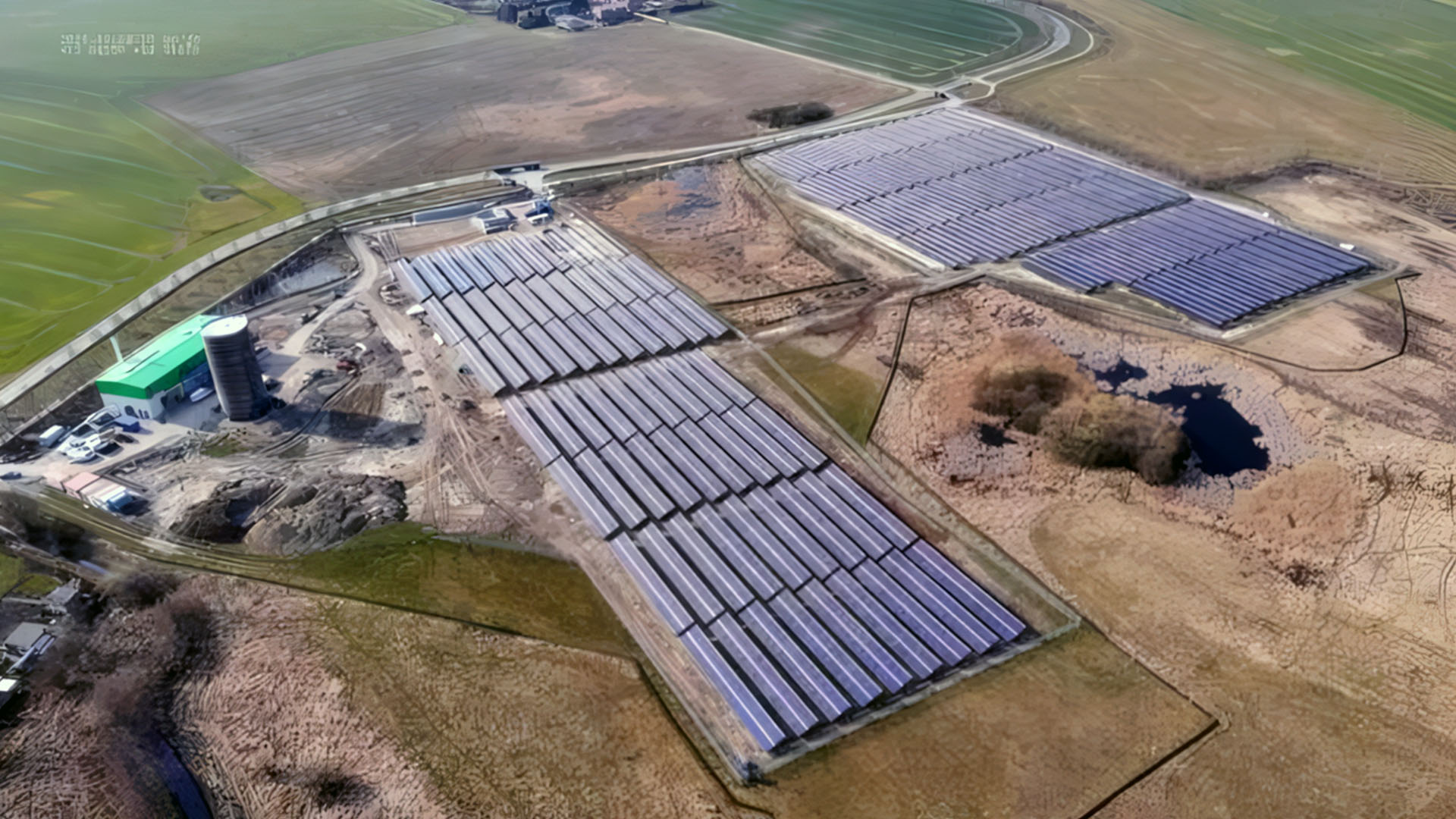 - Aerial view of a solar thermal plant with several large collector fields, an operations building and a cylindrical storage tank surrounded by agricultural land.