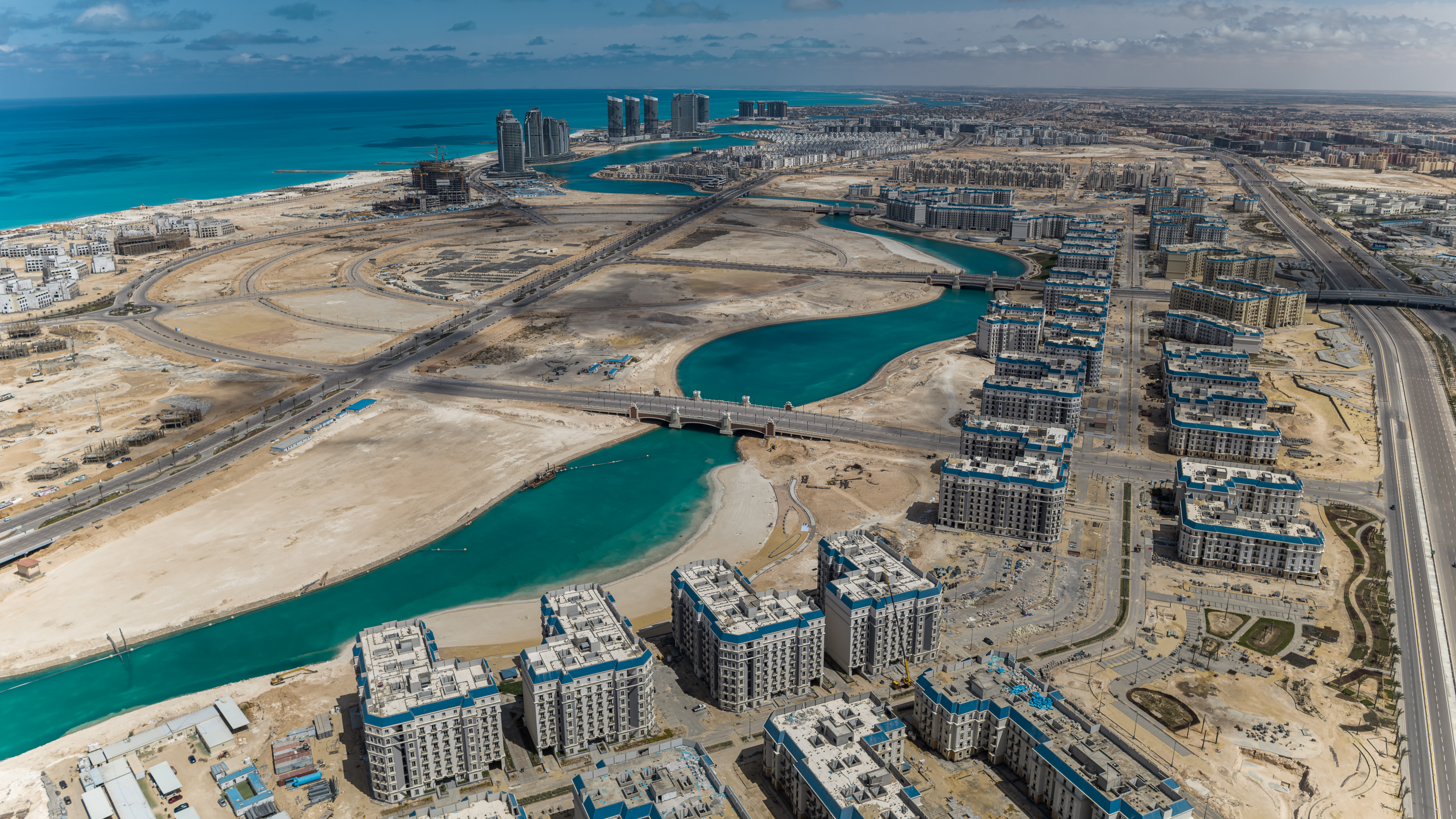  Luftaufnahme des Latin District mit Wohngebäuden entlang türkisfarbener Lagunen und Blick über New Al-Alamein bis zum Mittelmeer.