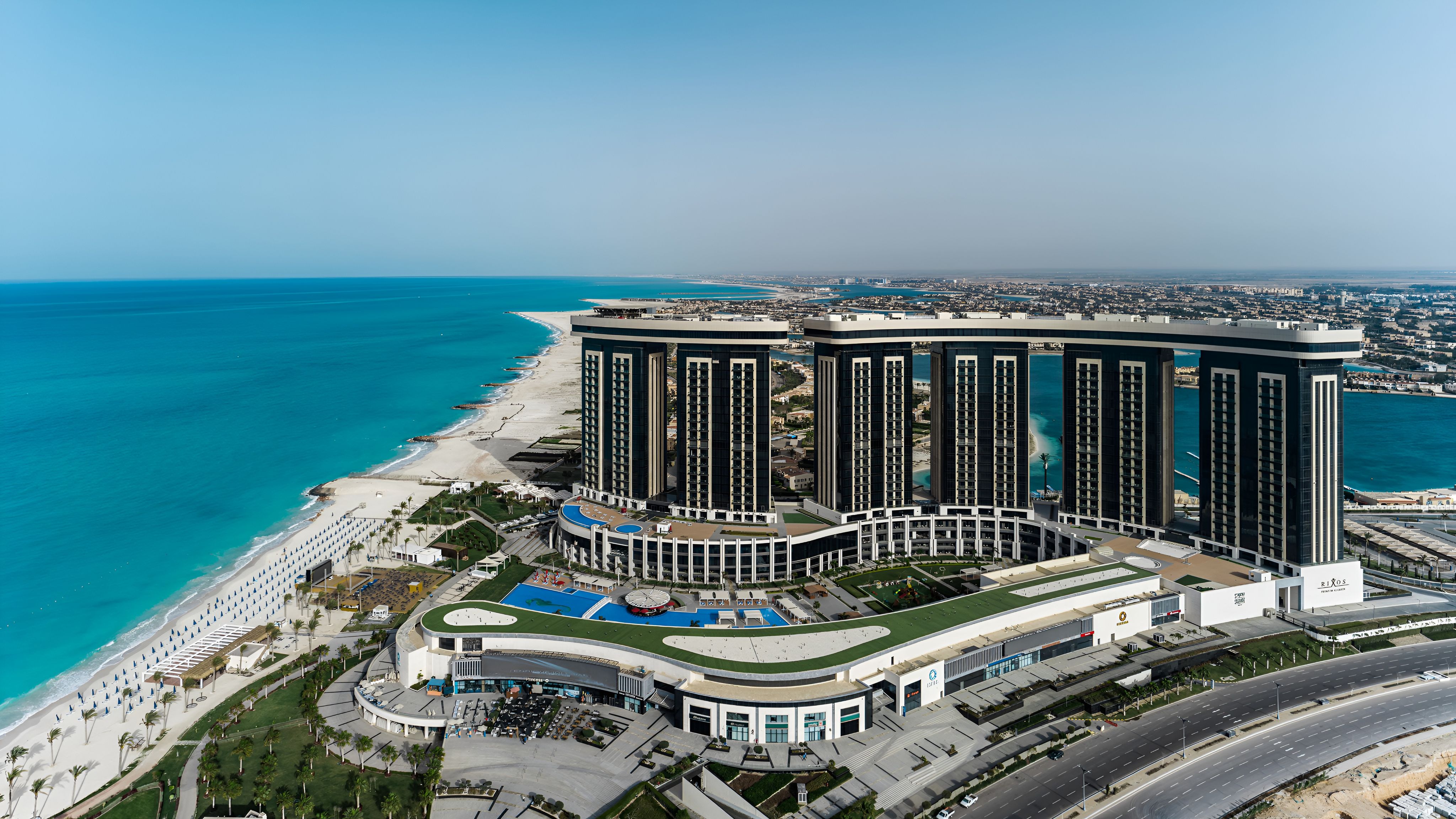 Luftaufnahme des Rixos Al Alamein mit mehreren Hoteltürmen, Pool- und Gartenanlagen sowie einem Strand am türkisblauen Mittelmeer.