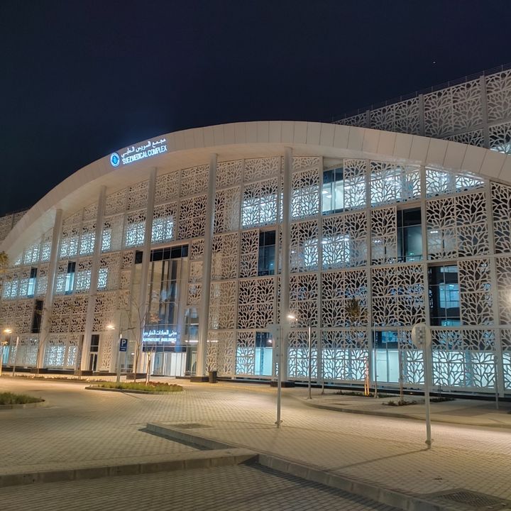 Beleuchtetes Ambulanzgebäude des Suez Medical Complex mit weißer Fassade und filigranen Sichtschutzpaneelen in organischem Muster.