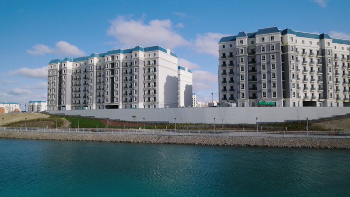 Wohngebäude des Latin District mit hellen Fassaden, blauen Dächern und Balkonen an einem Wasserlauf in New Al-Alamein.