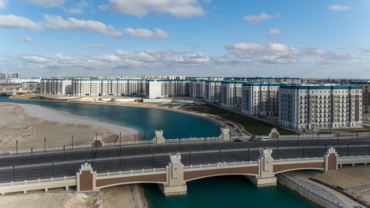 Luftaufnahme der Wohngebäude des Latin District entlang einer türkisfarbenen Lagune mit Straßen und einer Brücke im Vordergrund.