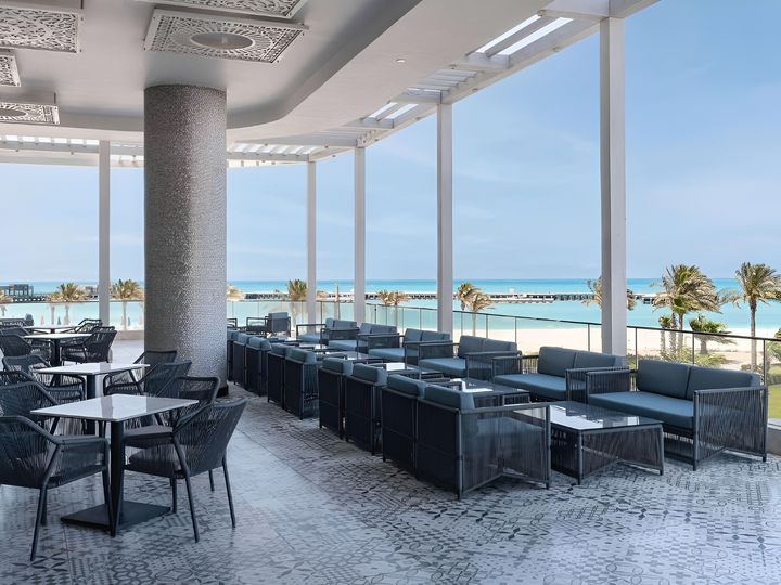 Überdachte Hotelterrasse mit Sitzgruppen und freiem Blick auf den Strand und das türkisfarbene Mittelmeer.
