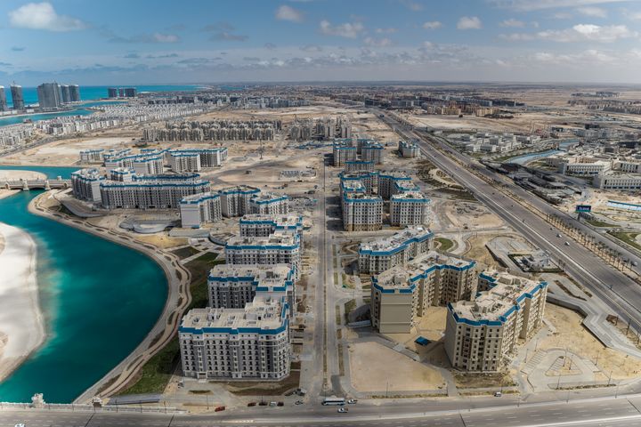 Luftaufnahme des Latin District mit Wohngebäuden beiderseits einer zentralen Straße, einer Lagune und weiteren Quartieren von New Al-Alamein.