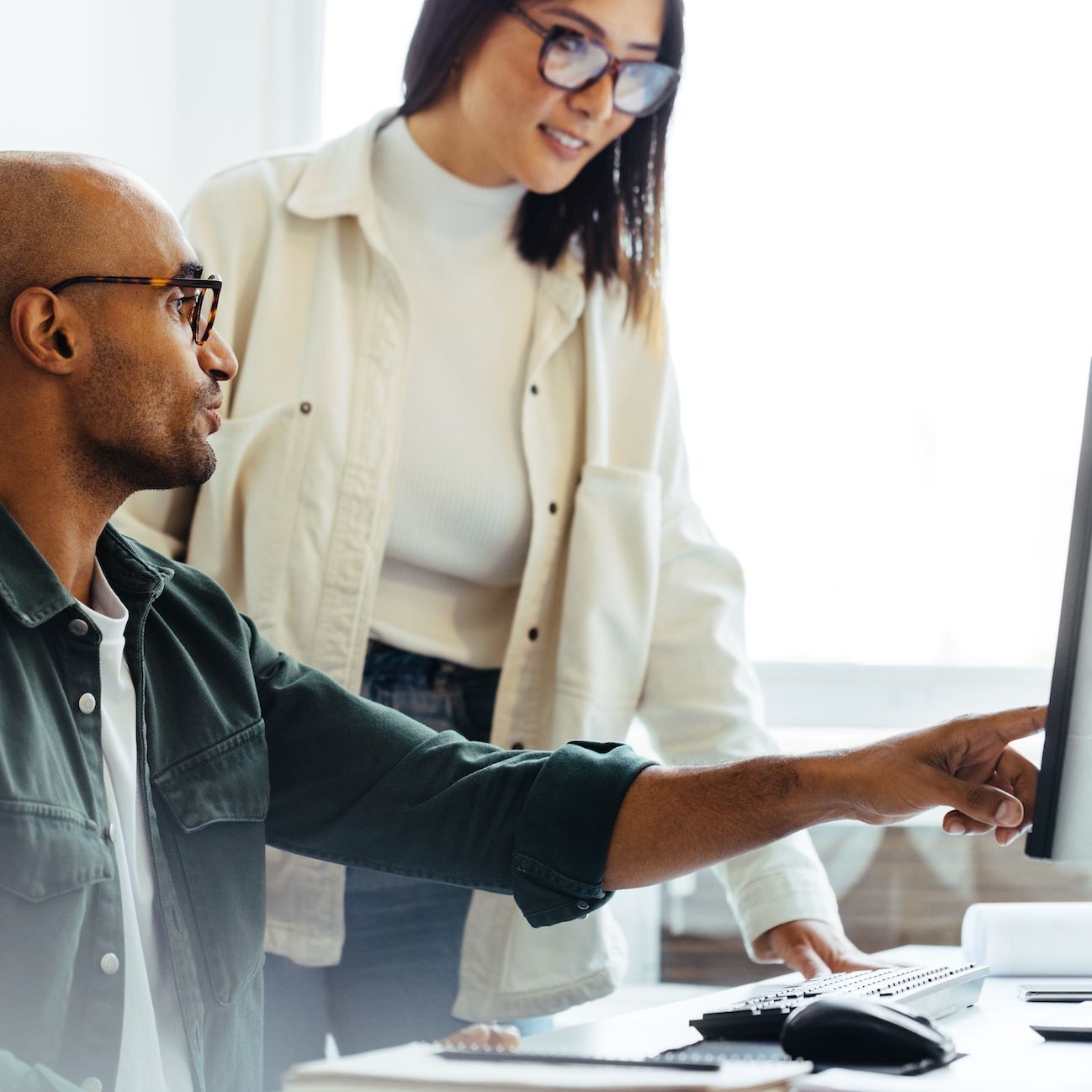 Two colleagues at a desktop, am an is showing a woman something on a screen