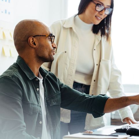 Two colleagues at a desktop, am an is showing a woman something on a screen