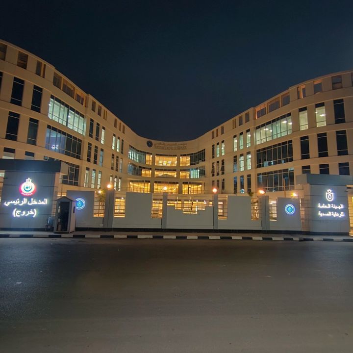 Nachtansicht des beleuchteten Haupteingangs des Suez Medical Complex, eingerahmt von geschwungenen Gebäudeflügeln und großen Fensterflächen.