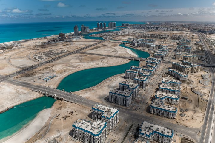Luftaufnahme des Latin District mit Wohnblöcken, Lagunen und Brücken sowie der Küstenentwicklung von New Al-Alamein im Hintergrund.