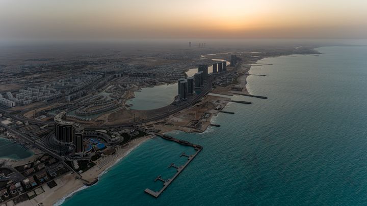 Weite Luftaufnahme der Küstenentwicklung von Al Alamein bei Sonnenuntergang mit dem Hotel, Lagunen, Wohngebieten und dem Mittelmeer.