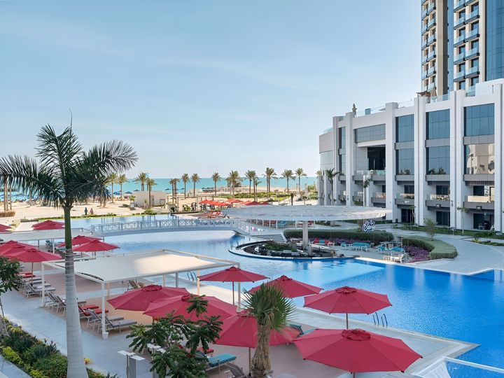 Poolbereich des Rixos Al Alamein mit roten Sonnenschirmen, Palmen und Blick auf den Strand und das Mittelmeer.