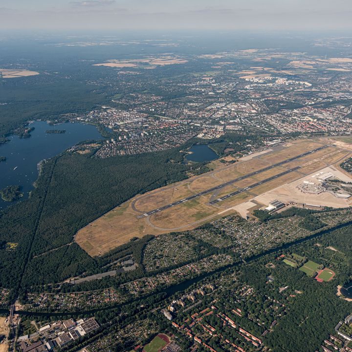 Luftaufnahme des ehemaligen Flughafens Berlin-Tegel mit Start- und Landebahn, Terminalgebäuden sowie den umliegenden Wäldern, Seen und Stadtgebieten.