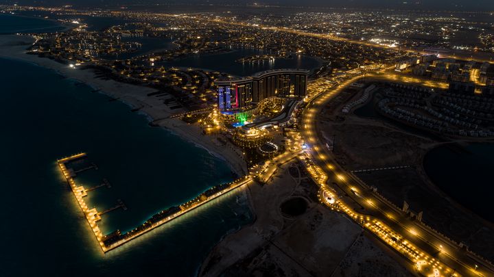 Nächtliche Luftaufnahme des beleuchteten Rixos Al Alamein an der Küste, umgeben von Straßen, Lagunen und Stadtvierteln.